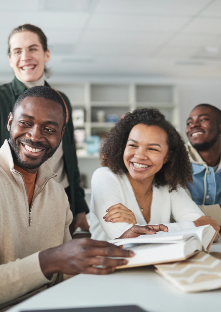 Three men and one women smiling and working together at a desk.
