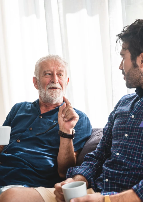 Older man talking to a younger man drinking a cup of tea.