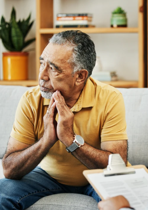 Older man sat on a sofa deep in thought.